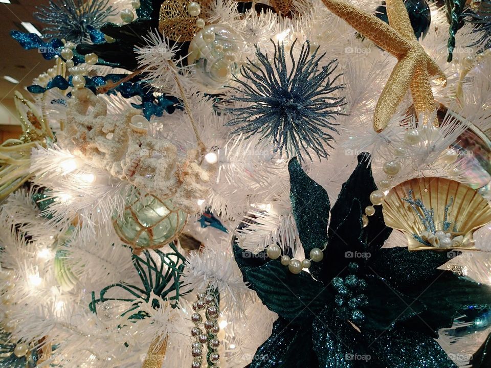 Gold and turquoise ornaments sparkling with glitter hanging from a white Christmas tree. 