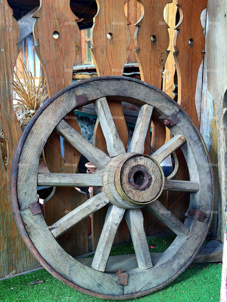 Circles.  An old round wooden wheel stands on a wooden porch with a green coating.