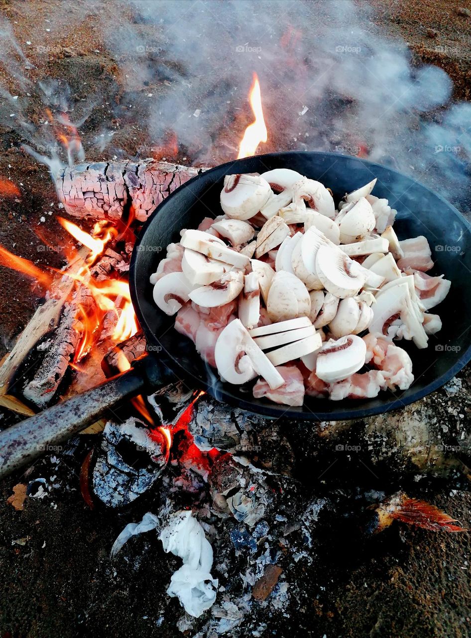 Bacon and mushrooms fried in a cast iron pan over a campfire. Ready to eat with patong.