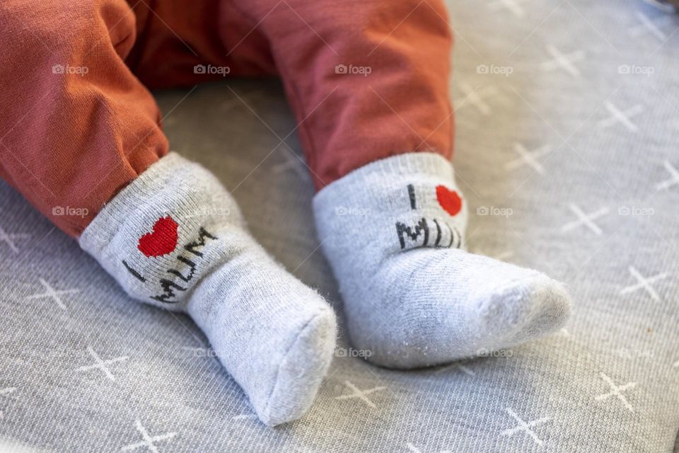 A close up portrait of the tiny feet of a cute little baby wearing I love mum socks.