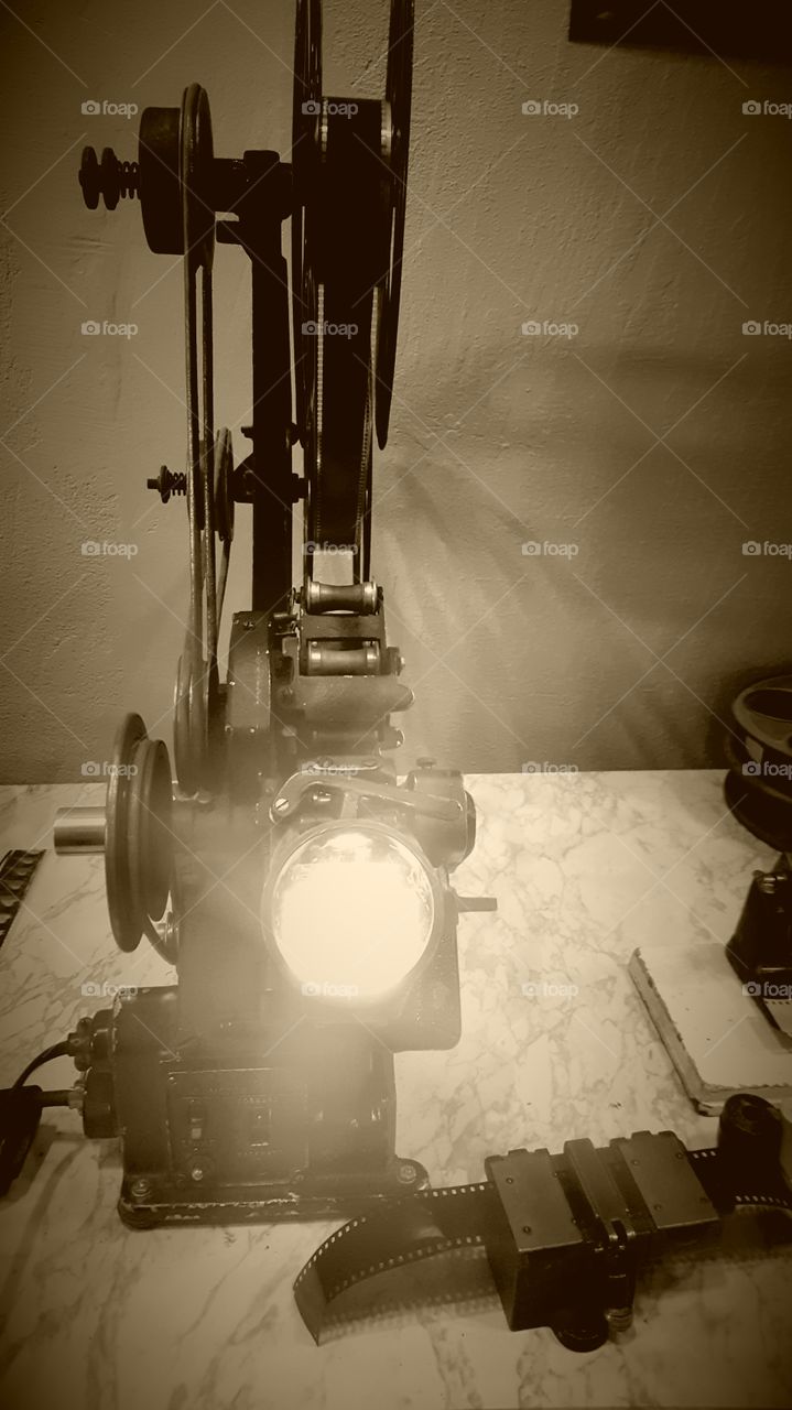 a vintage film projector or viewer possibly to view the film while editing. Photo taken at Niles Film Museum in sepia. Looks like it has power on but it is the sun and lights reflecting off the lens.