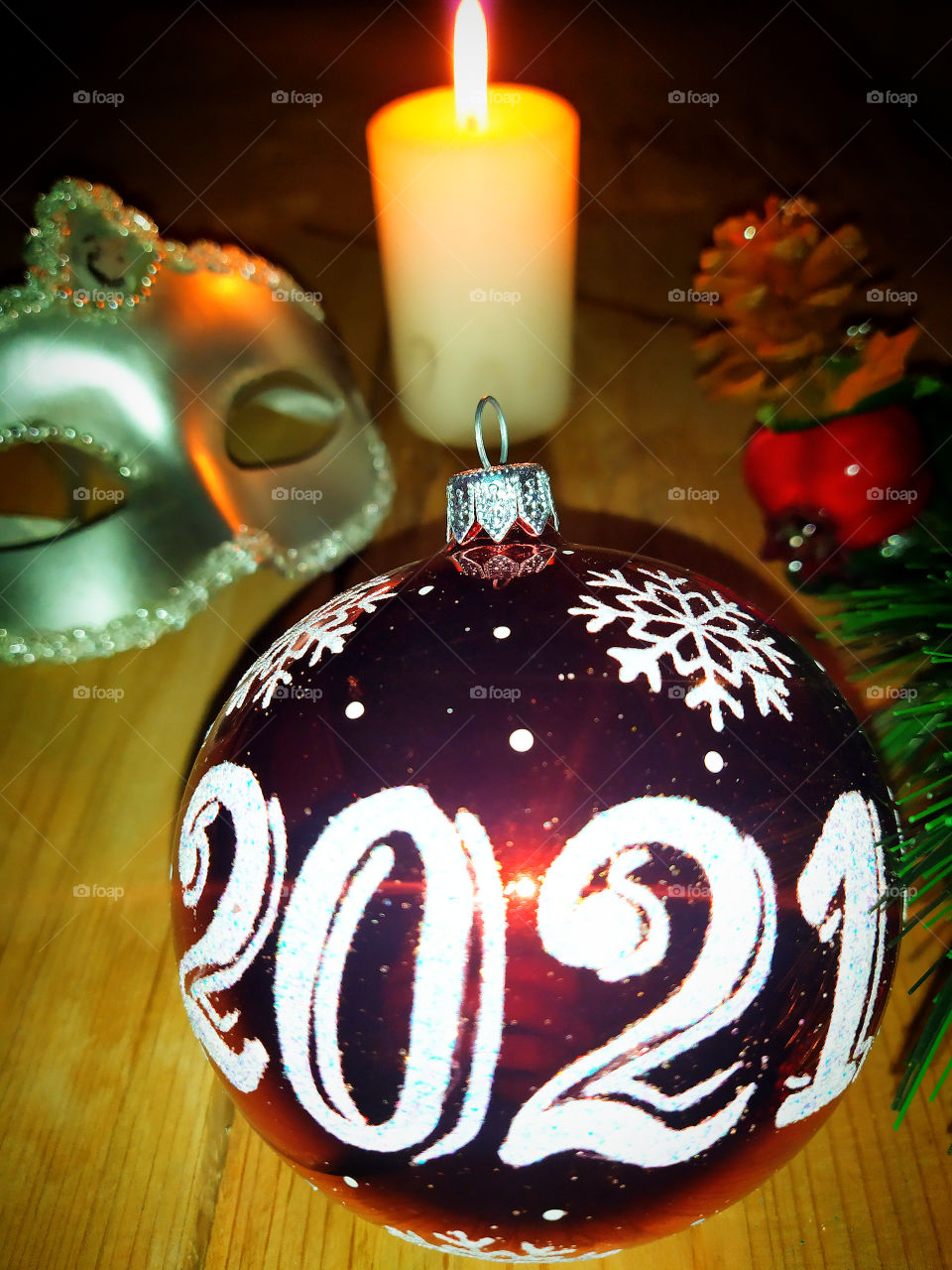 Christmas tree decoration. Glass ball with numbers "2021". Against the background of a green branch, a silvery masquerade mask and a candle that burns