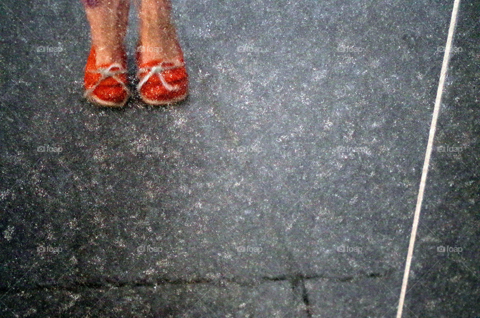 High angle view of standing human feet in orange coloured shoes reflected on grey wet surface in Budapest, Germany.