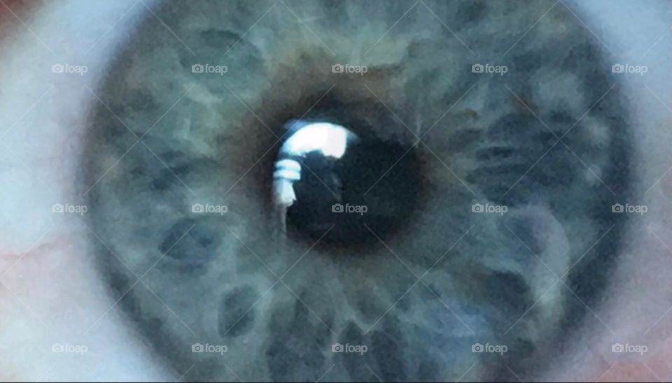 Timothy’s left eye seen extremely close showing much detail in the multifaceted patterning of the iris and a silhouetted mirror image reflecting in his pupil. Photographed in Bushwick, Brooklyn in 2017. Hypnotic Productions