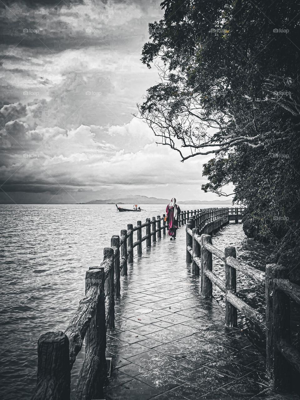 Pathway by the seaside and hilly forest and a lady in red is walking by