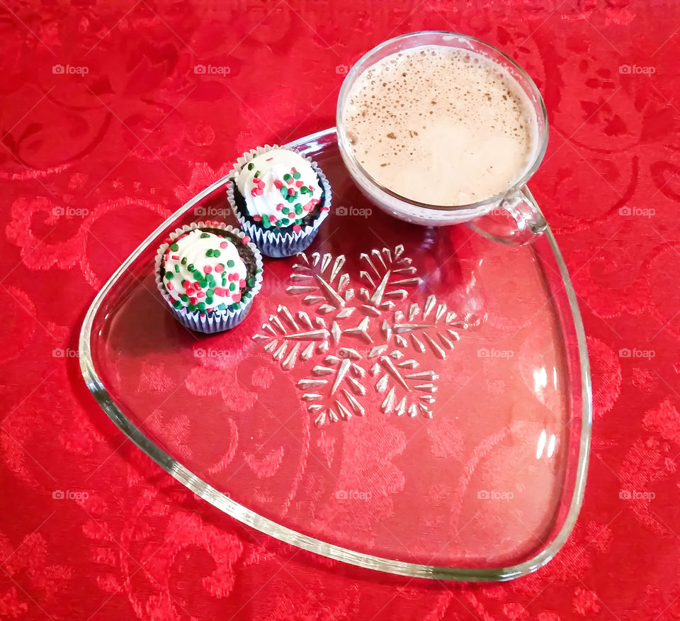 Cappuccino and two Christmas cupcakes on a snow flake plate against a red background