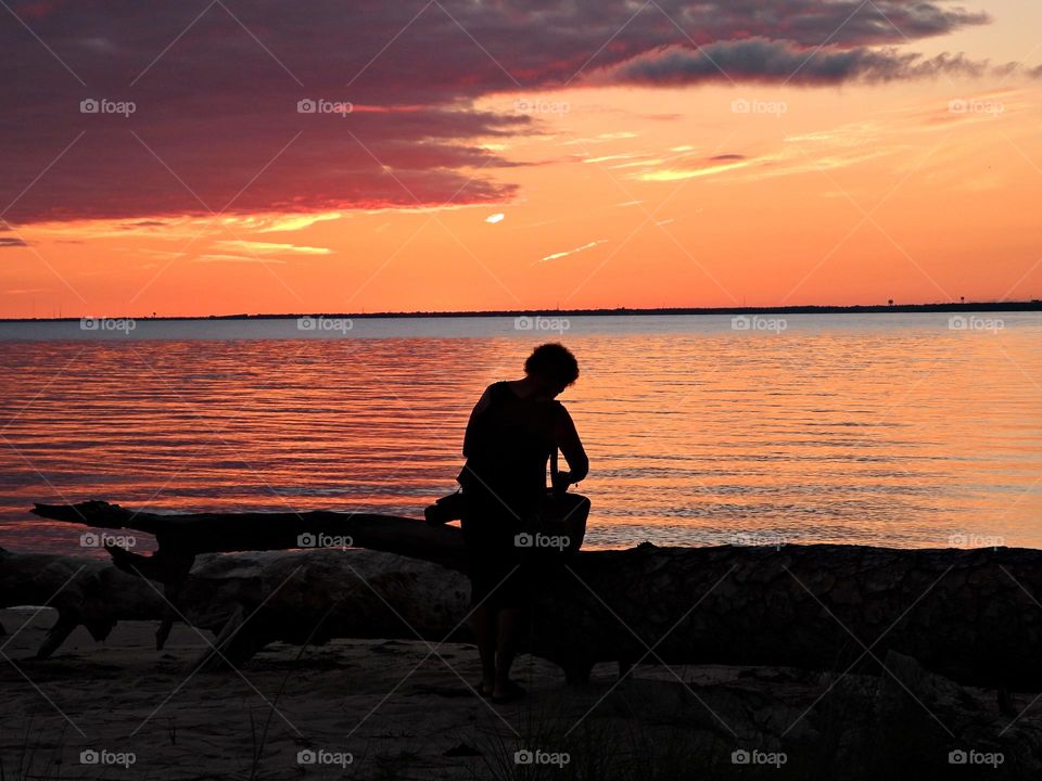 A young lady is setting up for the last light of the night. The big orange and crimson ball slowly going down and down and it sets into the horizon making the sky absolutely stunning.