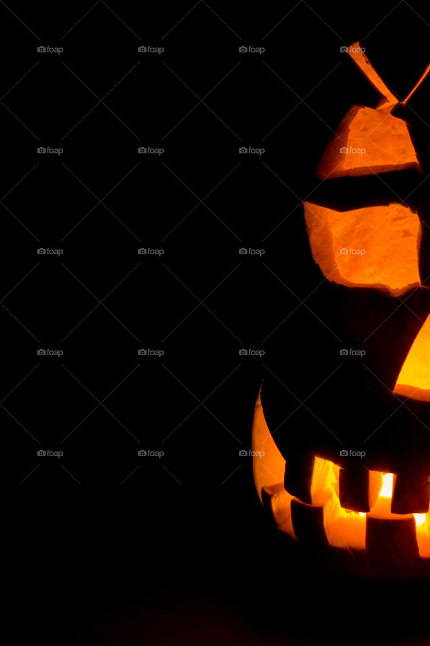 Half of an evil pumpkin close-up glowing in a dark room.