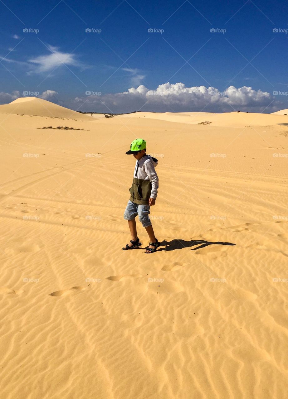 A boy is standing in the middle of the sand, the sand is prominent with pale yellow and the color of the blue sky,white clouds
