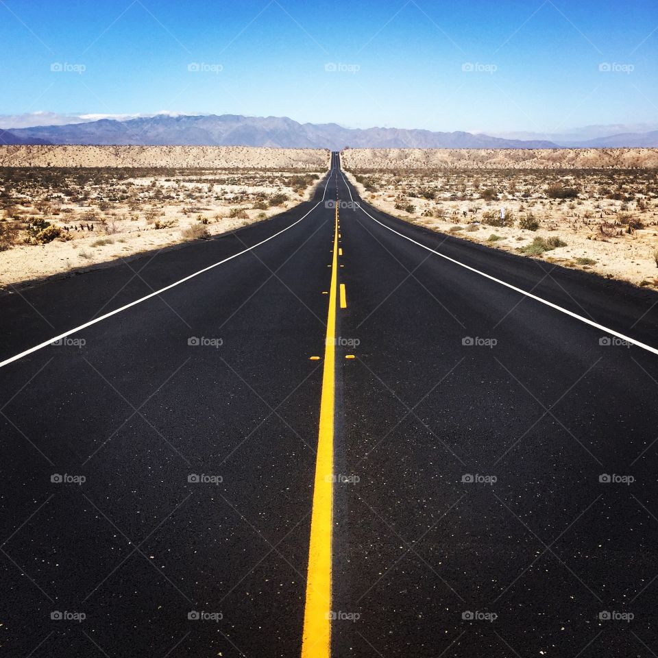 Empty road by mountains against clear sky