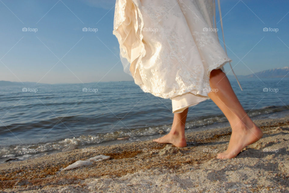 legs and feet of a bride in her wedding dress walking into a lake - the water trails off into the horizon in the distance