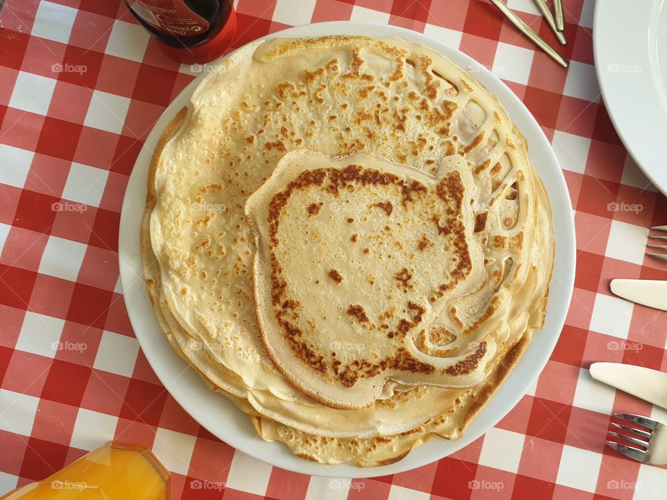 A top down portrait of a stack of pancakes lying on a plate on a checkered table cloth on a table, ready to be eaten by whomever wants an unhealthy delicious snack.