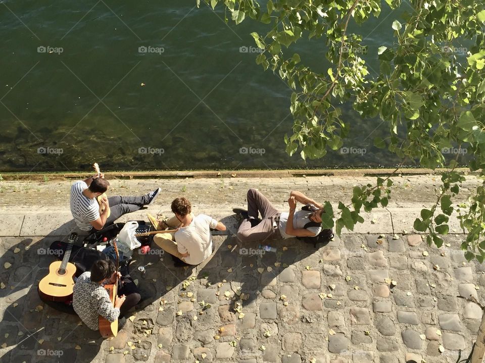 Boys playing guitars, friends playing music instruments on the banks of the Seine river in Paris, France, people spending time outdoors, guys having fun together 