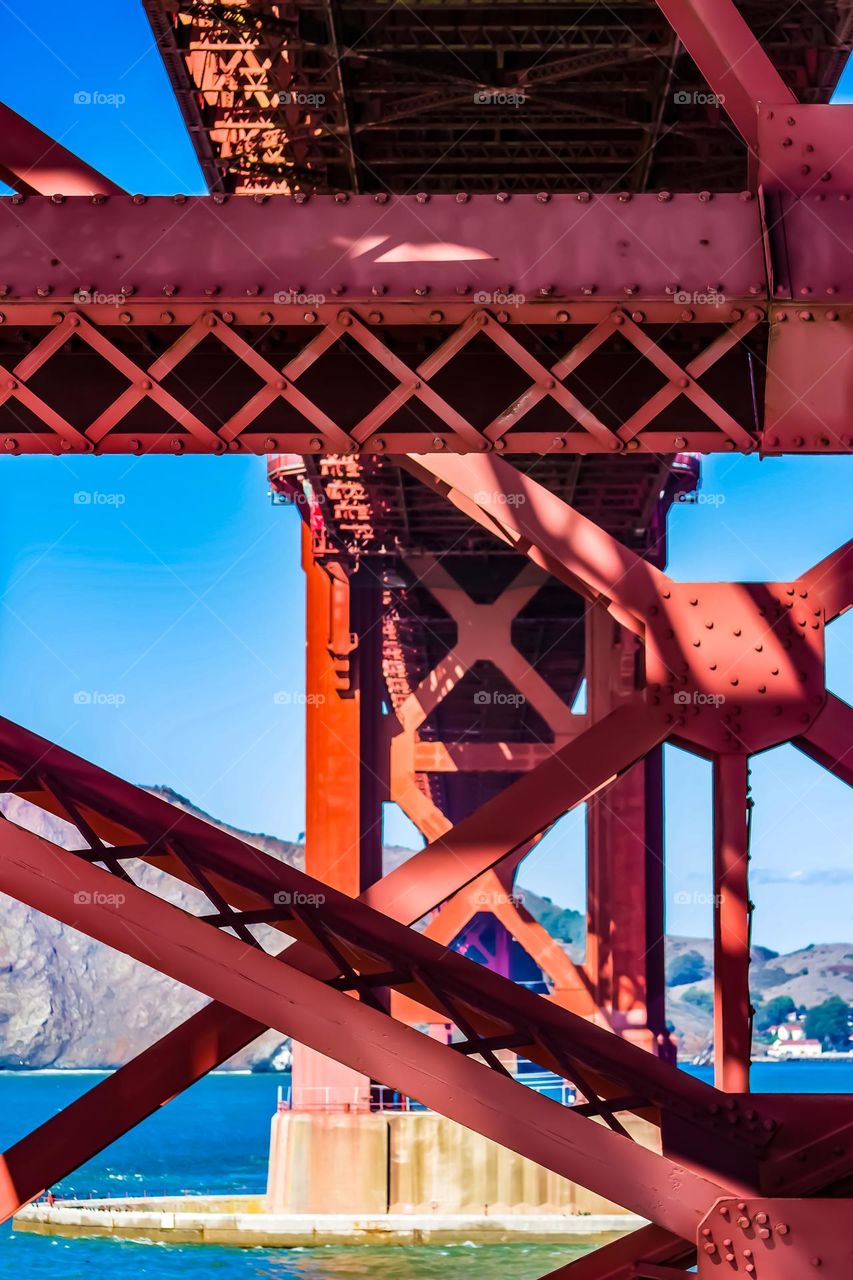 View under the Golden Gate Bridge from on top of Fort Point in San Francisco California, showing the steel beams crisscrossing and slight views of the Pacific Ocean