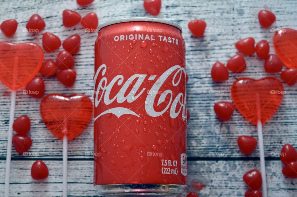 A can of original Coca-Cola with candy hearts and a white rustic background