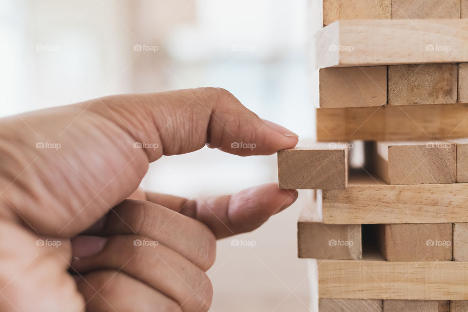 Close up left hand of man take the wooden stick out of the wooden tower (Jenga)