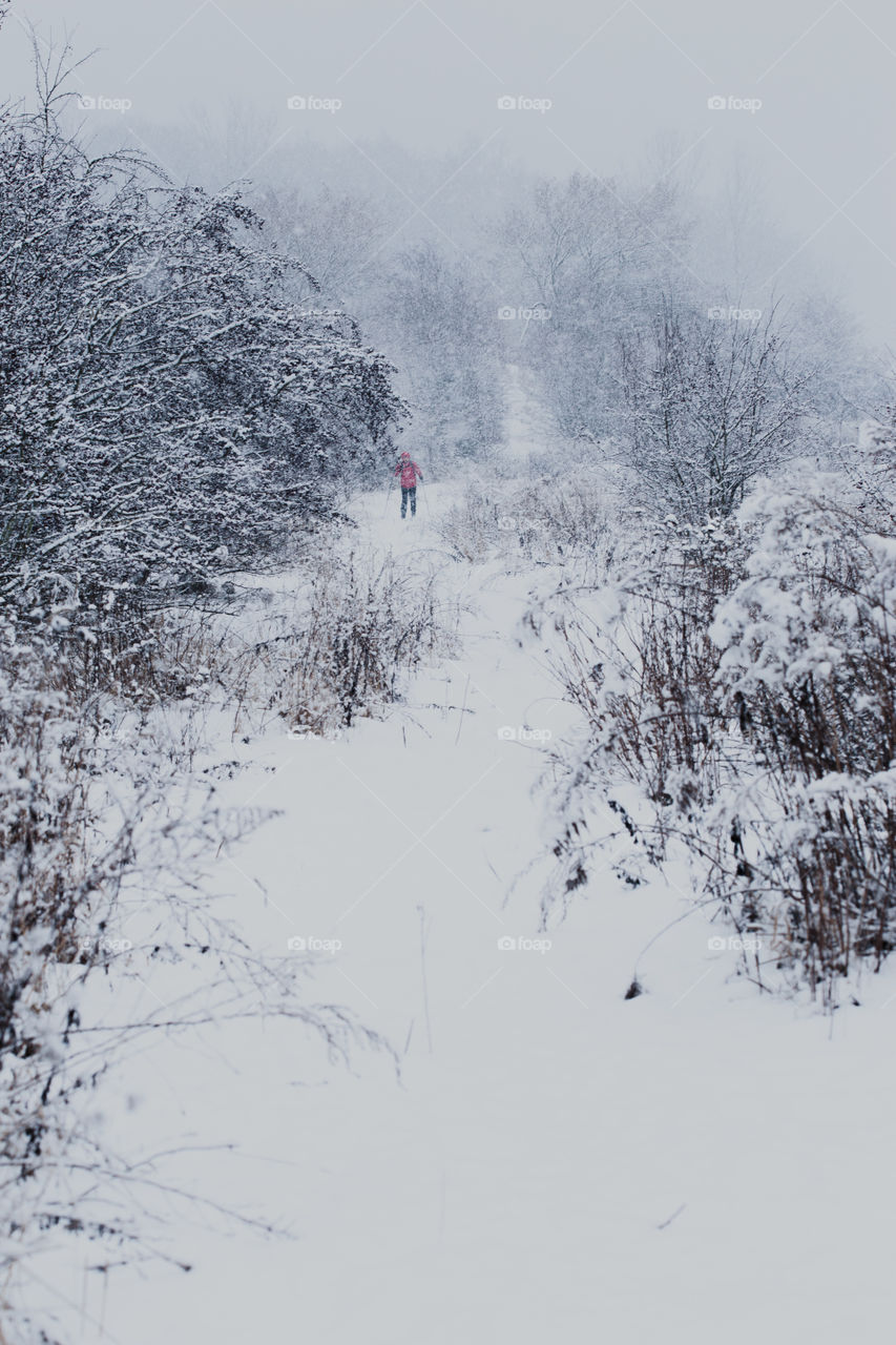 Young man jogging through meadow pathway during heavy snowing. Workout outdoors during winter snow storm