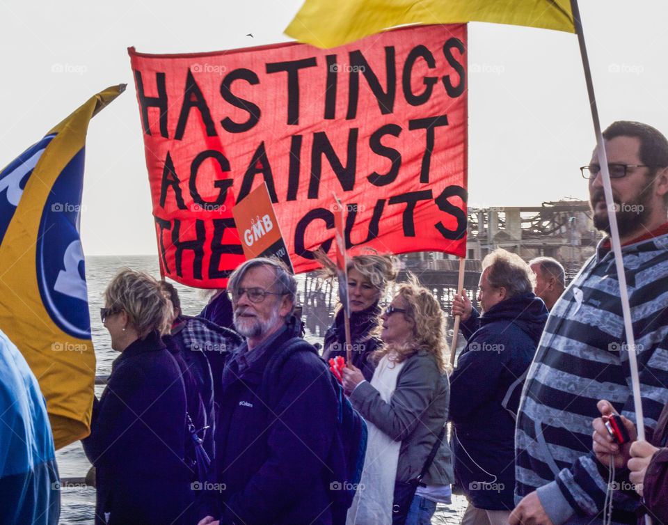 A large red “Hastings against the cuts” banner is held aloft by protesters - November 2011