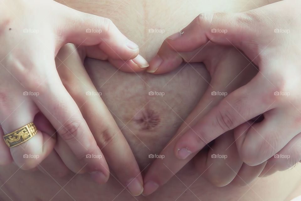 Close-up of couples hands forming heart shape on pregnant belly