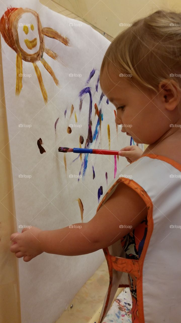 Little girl painting with brush on canvas