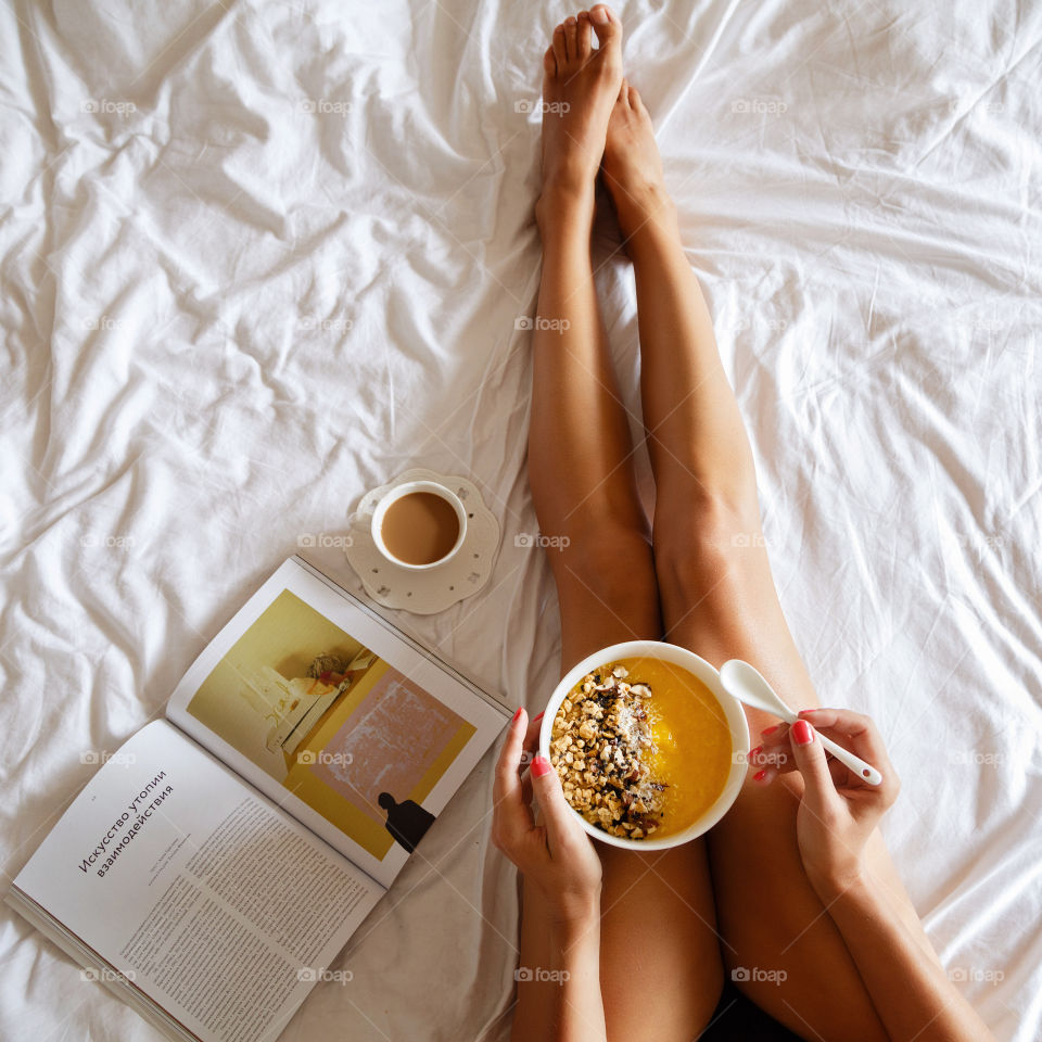 Woman eating granola with fresh fruits on the bed