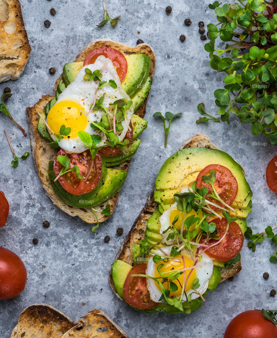 Two toasts with avocado, fried eggs and tomatoes.