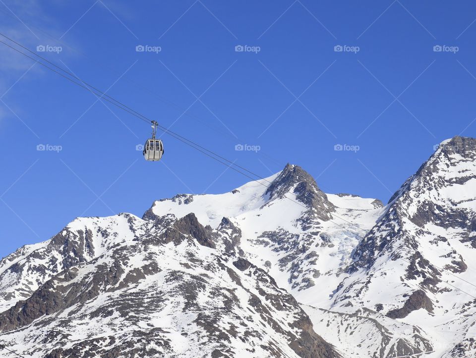 Gondola against blue sky in front of snow mountains.