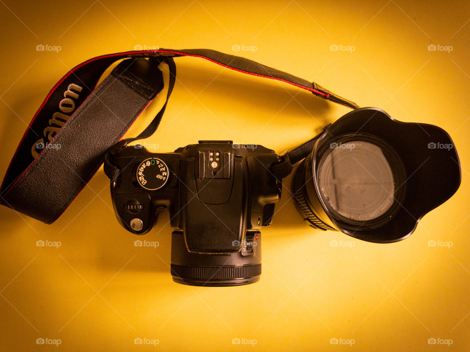 Canon camera with a lense and a strap on a yellow surface with a lot of shadows.