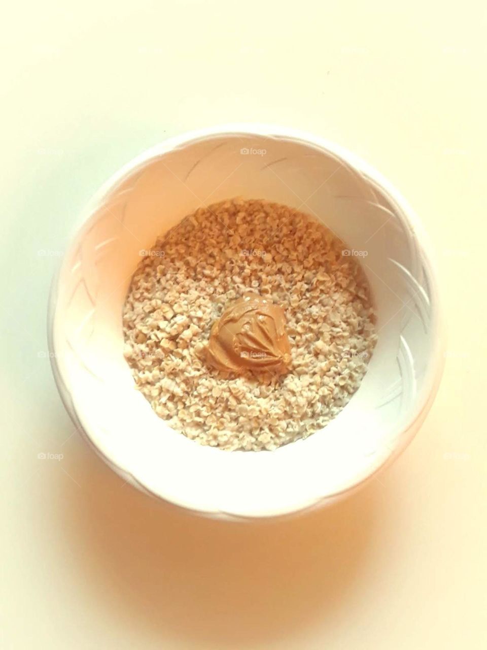 A bowl of oatmeal with a spoonful of peanut butter in the center and the bowl is on an off white background.