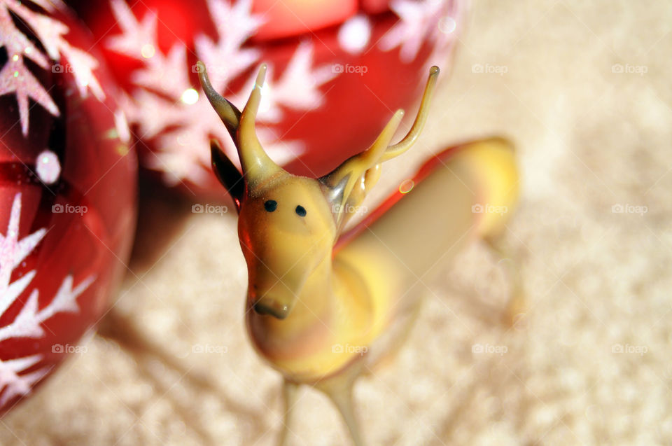 Vintage glass reindeer with Christmas tree ornament in background.