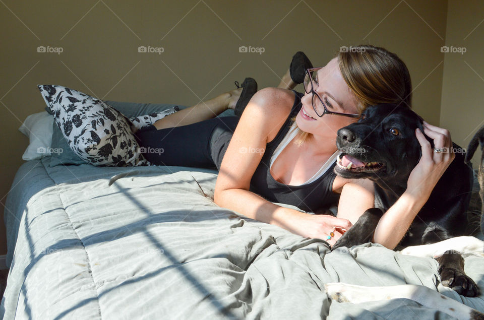 Woman smiling and lounging with her dog on a bed