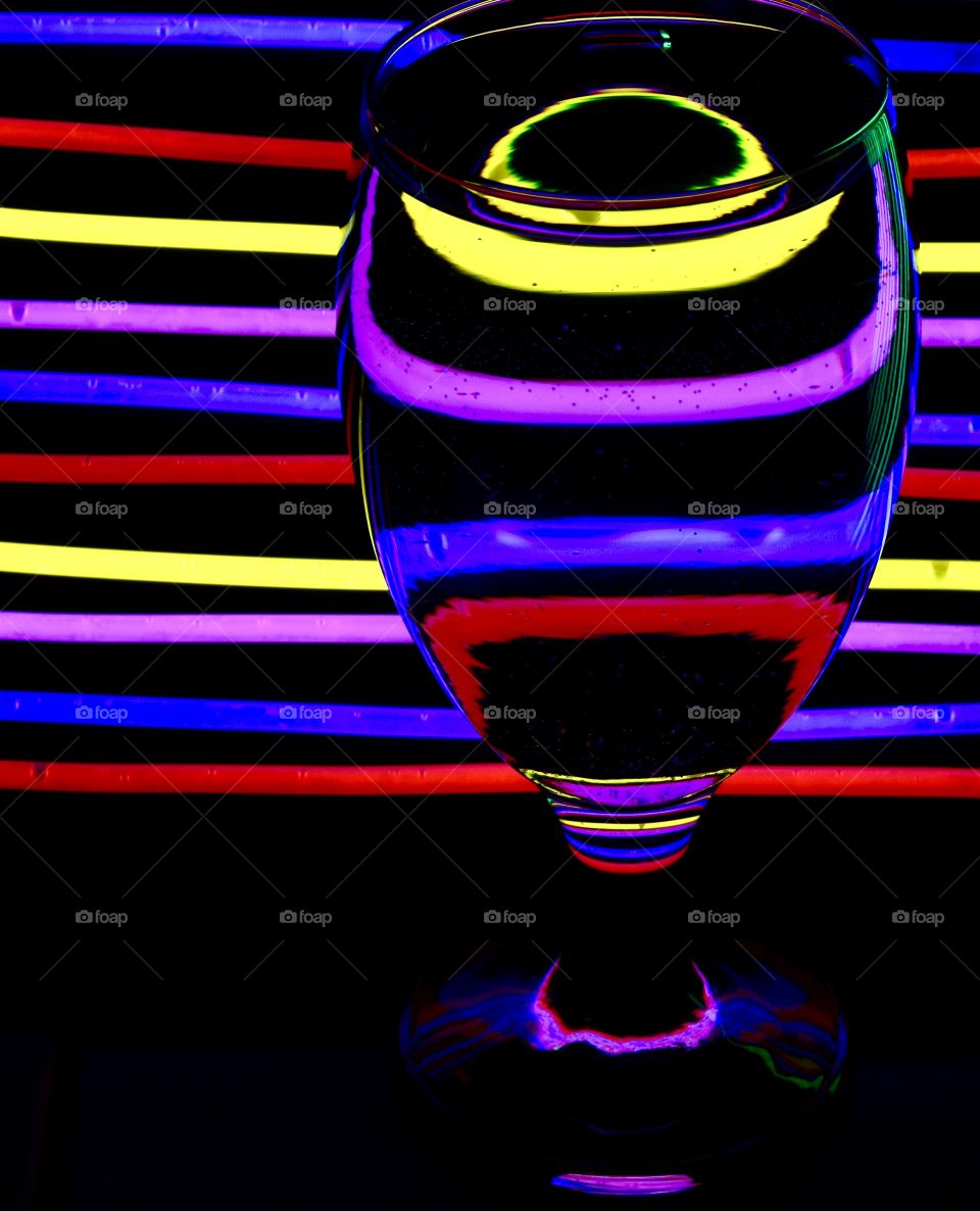 Glow sticks on a black background with a goblet filled with water to create a distorted look