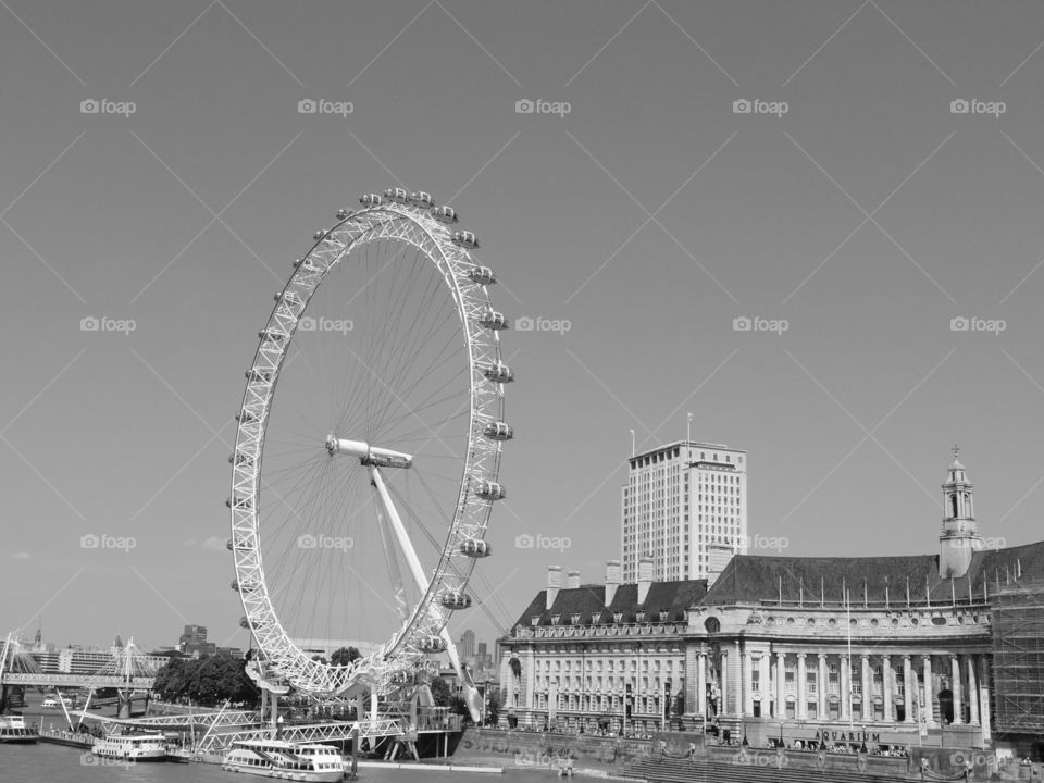 The London Eye towers above local historic buildings in London on a sunny summer day. 