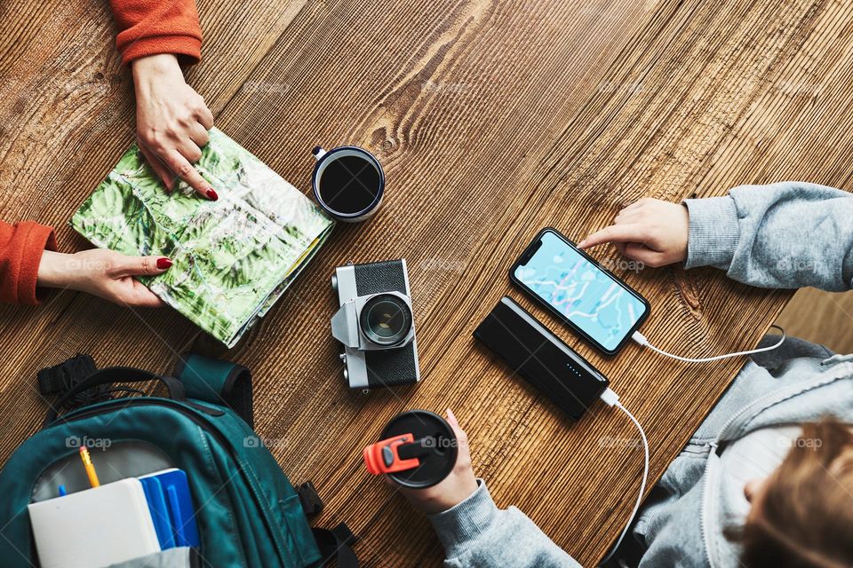 Family planning vacation trip. Girl searching travel destination and routes using navigation map on mobile phone. Woman pointing on paper map. Charging smartphone with power bank. Using technology while travelling