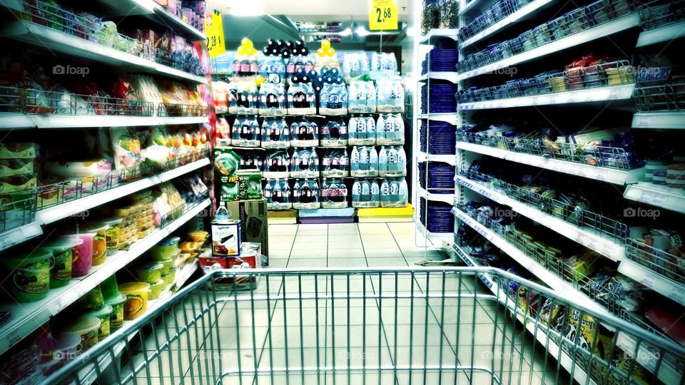 Supermarket cart being pushed between the  racks of groceries 