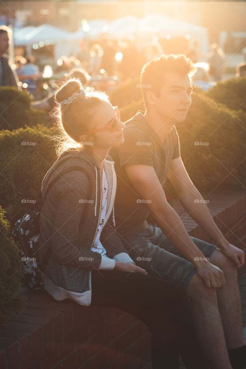 Couple of friends, teenage girl and boy,  having fun together, sitting in center of town, spending time together