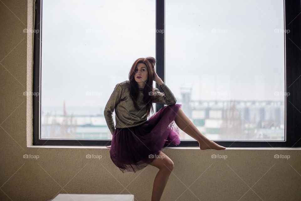 Beautiful girl in skirt seats on the windowsill 