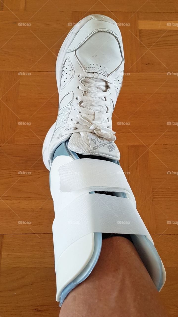 White ankle stabilizer with shoe helps to stabilize injured foot and tendon, rehabilitation - fotledsskydd stabiliserar skadad fot och fotled, rehabilitering