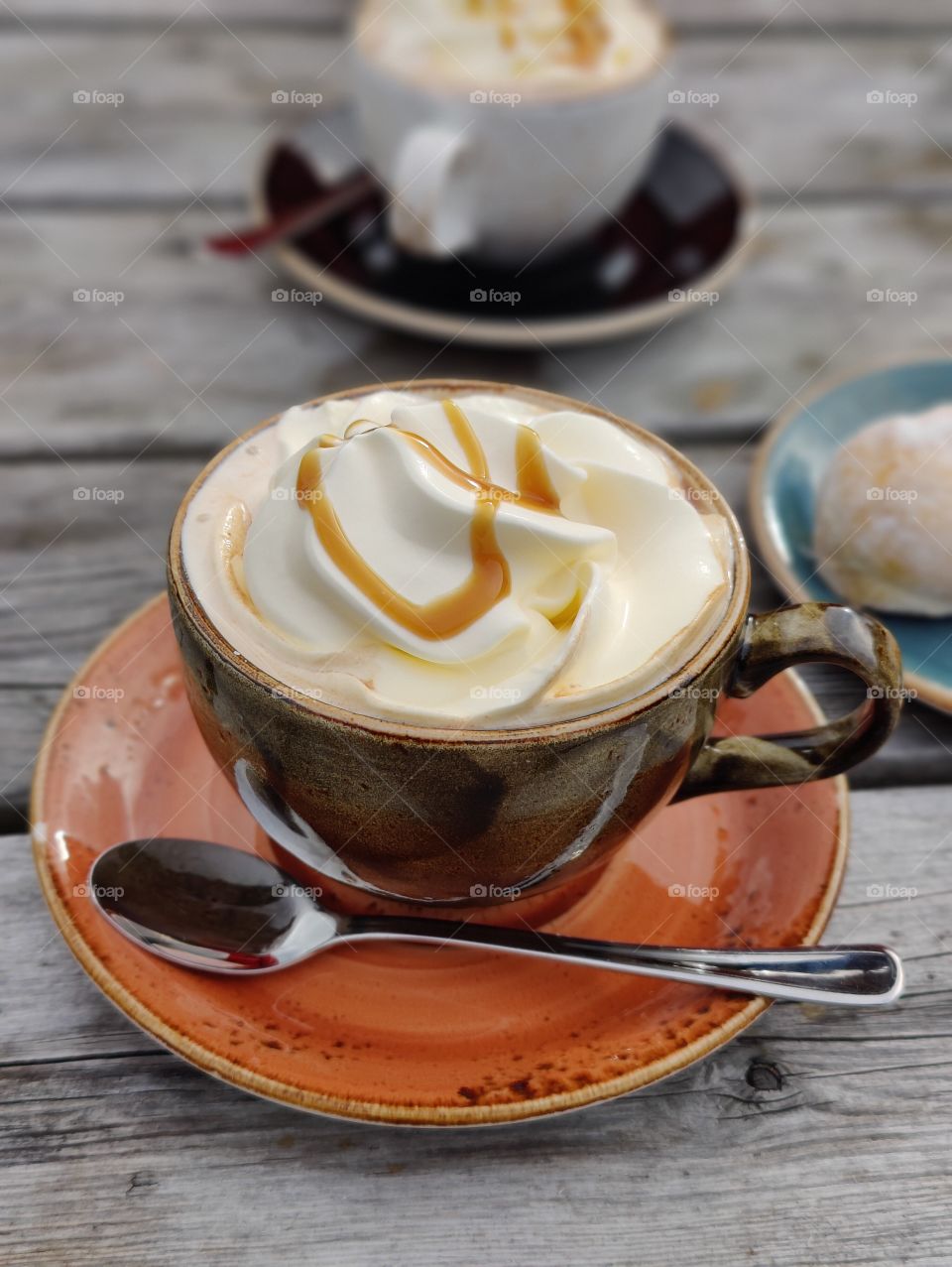 Coffee with cream and caramel in brown cup and orange saucer including silver spoon