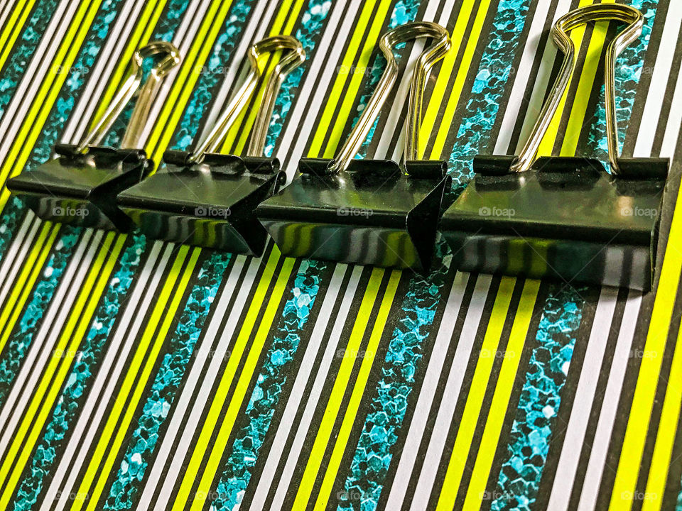 Black binder clips on striped paper. The flat rectangular part of the clip is reflecting the lines of the paper making more little rectangles in the reflection. 