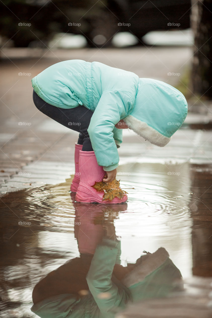 Little girl in rubber boots playing in puddle