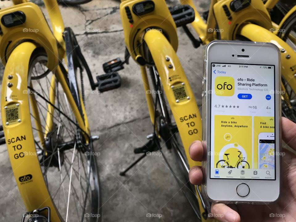 user is using mobile application in iphone SE for renting bicycle of ofo brand on street at old town, phuket, thailand