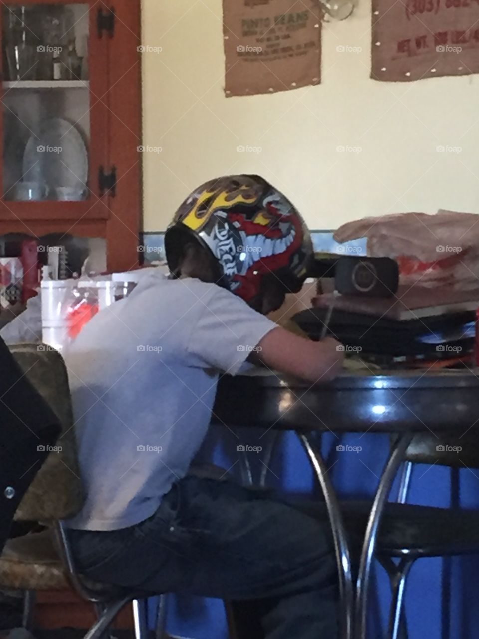 Mixing business and pleasure.  Finishing his homework before he goes out to ride.  Rockin the helmet all the while