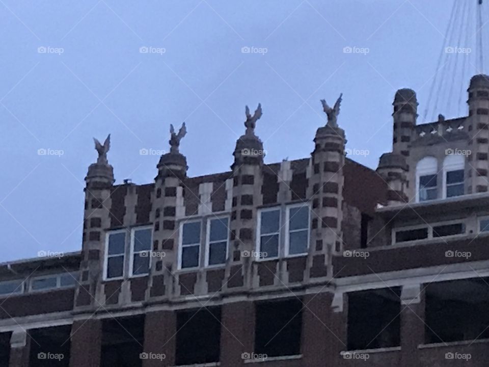The top of a creepy brick building with windows and four gargoyles on top at dawn