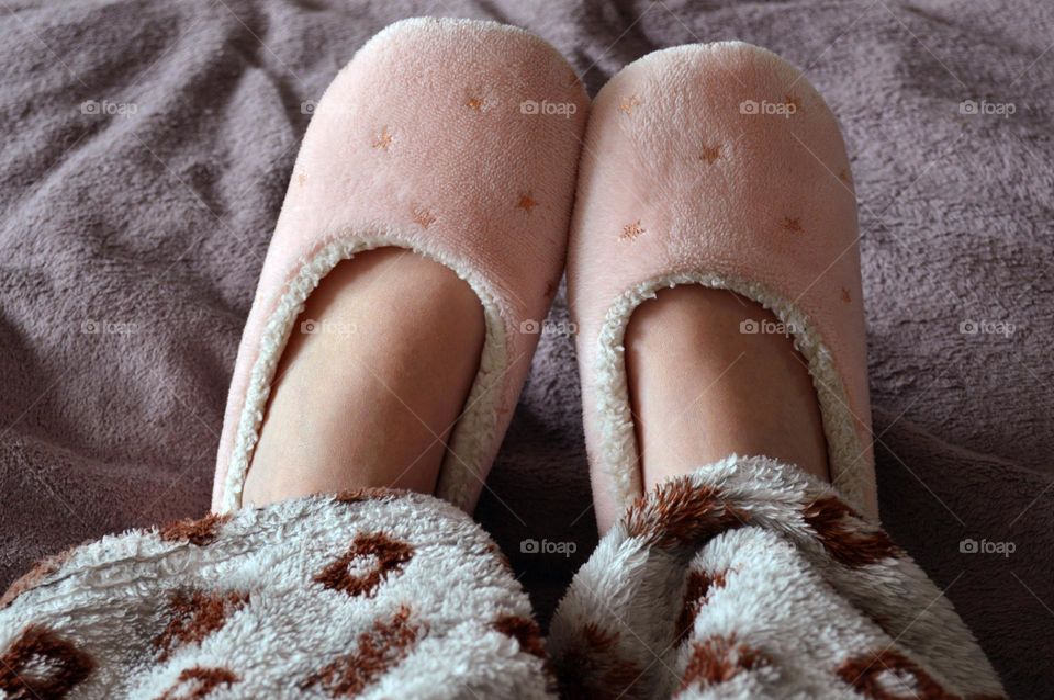 Girl on the bed in warm home slippers and rhombus print pajamas, home comfort and coziness