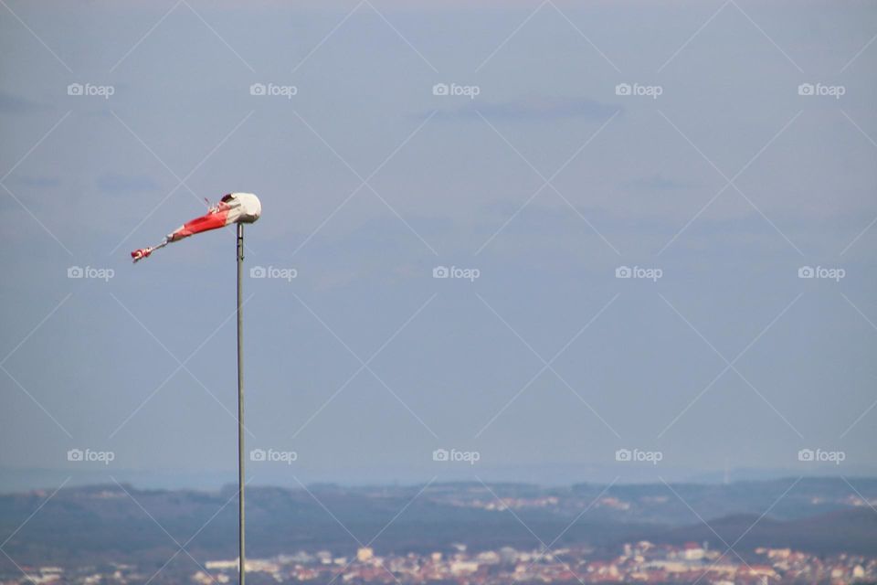 Red and white striped windsock flag in strong winds in front of a village view