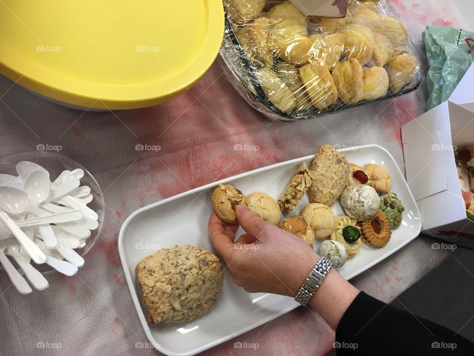 Woman putting fresh Italian cookies on platter next to homemade sandwiches preparing for a party 