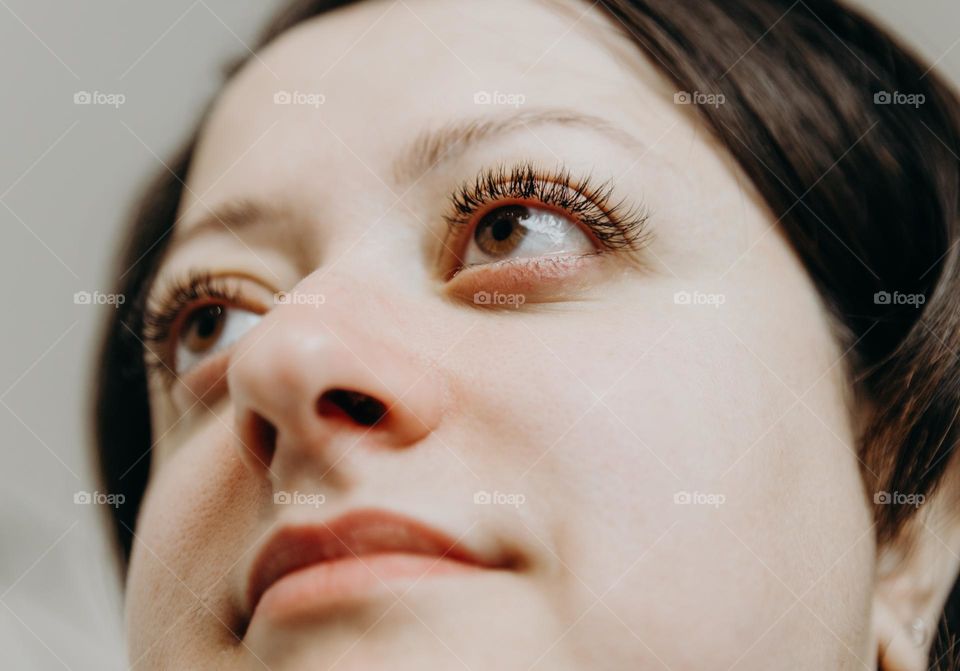 Portrait of face of one beautiful Caucasian happy brunette girl looking away on summer day, view from bottom up close-up with selective focus.