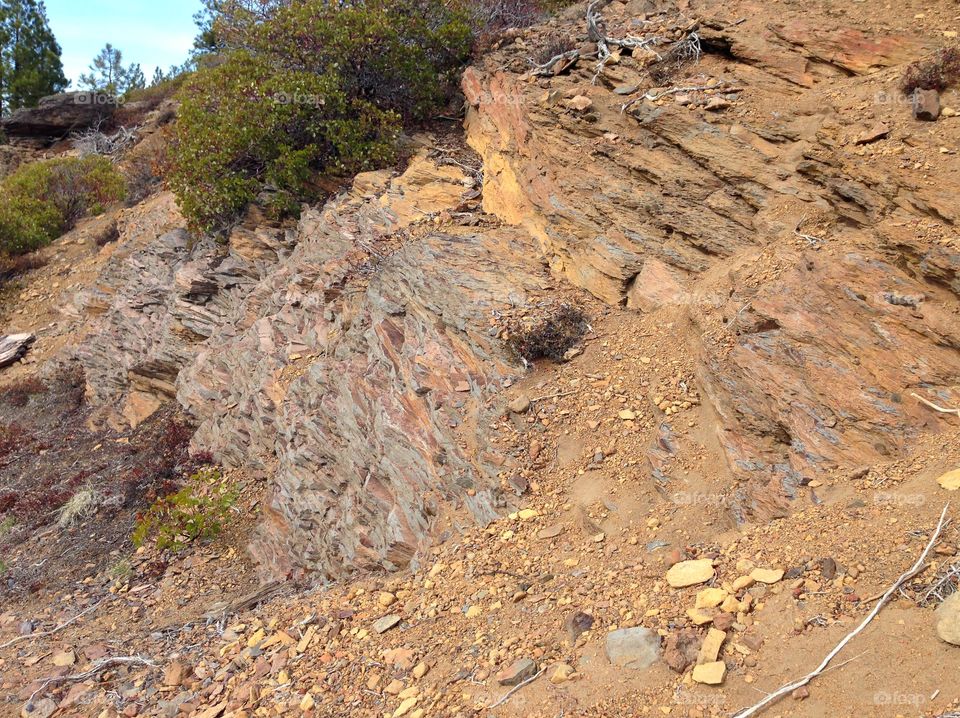 Rough layers of beautiful reddish brown rock and manzanita bushes on a hillside in Central Oregon on a sunny day. 