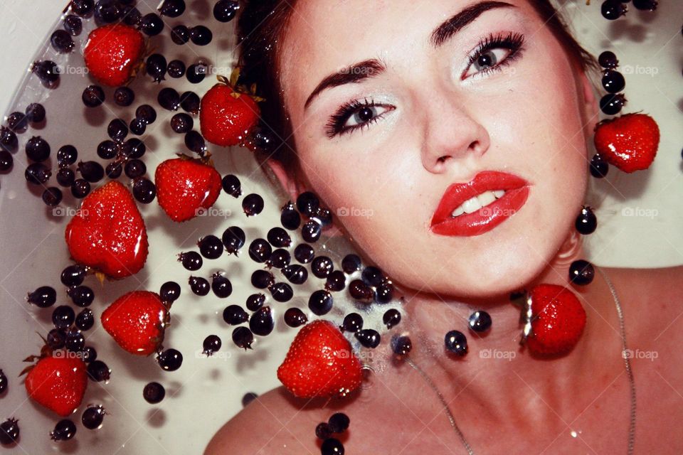 Woman in bathtub with berries floating on water